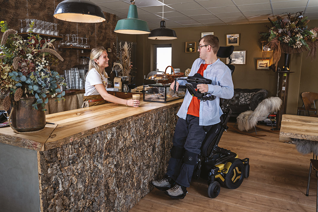 Permobil M Corpus VS, Gold in colour being used in a Cafe. Beyond Mobility. 